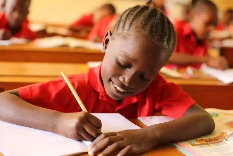 boy in orange shirt writing on white paper